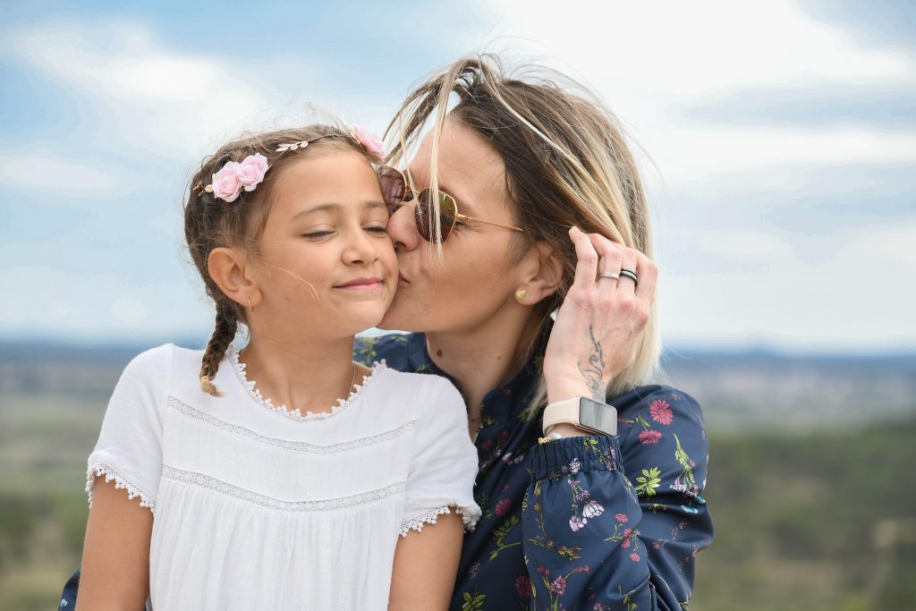 photo d'une mère qui embrasse sa fille avec en fond la plage